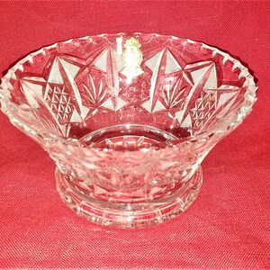 May include: A clear glass bowl with a cut crystal design. The bowl has a scalloped edge and a round base. The bowl is on a red background.