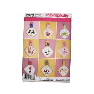 May include: A Simplicity sewing pattern envelope 2670 featuring illustrations of nine square baby security blankets with pacifier clips. Each blanket displays a different embroidered character including a dog, bear, frog, rabbit, penguin, and mushroom.