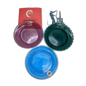 May include: Three decorative plates in purple, green, and blue with scalloped edges. A red card with the word "Cranberry" is visible. A metal silhouette of a person working is also present.