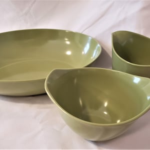 May include: A set of three green bowls, including a large oval bowl, a smaller round bowl, and a gravy boat with a handle.