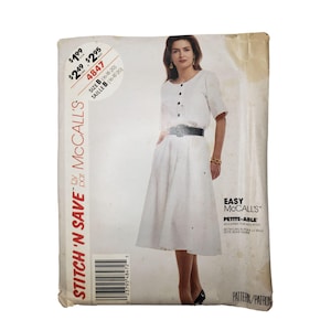 May include: A McCall's sewing pattern featuring a woman wearing a white dress with a button-up top and a pleated skirt. The pattern is labeled "Easy" and "Petite-Able". The package has a price tag and the text "Stitch 'N Save".