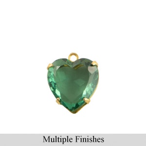 以下が含まれることがあります： ファセット加工が施されたエメラルドグリーンの宝石が付いた、ハート型のペンダント。 宝石は、吊り下げ用の小さなループが付いた金色の金属フレームにセットされています。 下部には「Multiple Finishes」というテキストがあります。