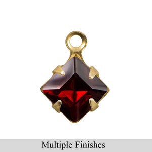 May include: A gold-toned pendant with a red square-shaped gemstone. The pendant has a loop at the top for attaching to a chain or cord.
