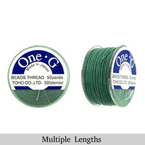 May include: A spool of green thread labeled "One • G Beads Thread 50yards TOHO CO.,LTD. 300denier" with the text "Made in Japan" on the label.