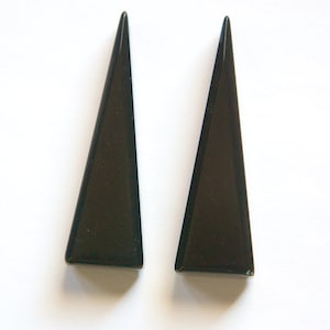 Puede incluir: Un par de pendientes negros en forma de triángulo.