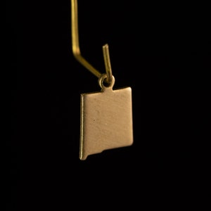 May include: Gold charm in the shape of the state of New Mexico. The charm has a loop at the top for attaching to a necklace or bracelet.