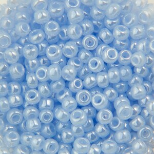 以下が含まれることがあります： 薄い青色のビーズが大量に写っているクローズアップ。ビーズは丸く、わずかに虹色の光沢があります。