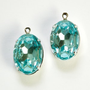 May include: Two turquoise blue oval-shaped glass rhinestones with silver settings and loops for hanging.