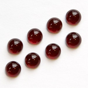 May include: Eight round, red, glass cabochons, also known as gemstones, on a white background.