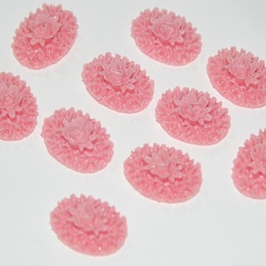 May include: Ten pink oval-shaped resin cabochons with a raised floral design. Each cabochon features a central flower surrounded by smaller flowers.