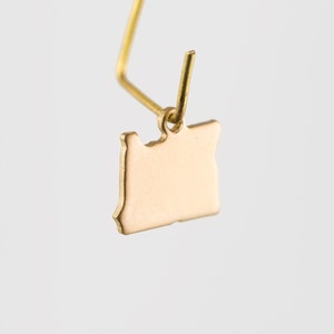 May include: Gold-colored earring featuring a state of Oregon silhouette charm.