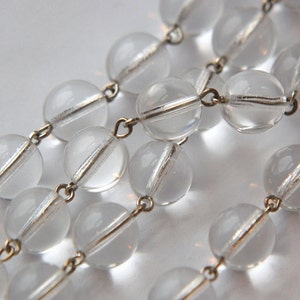 May include: A strand of clear glass beads with gold-toned metal connectors. The beads are round and have a slight shimmer.