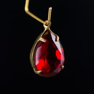 Pode incluir: Um brinco de pedra preciosa vermelha em forma de lágrima com engaste de ouro.