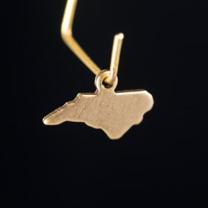 May include: Gold earring featuring a cutout of the state of North Carolina.