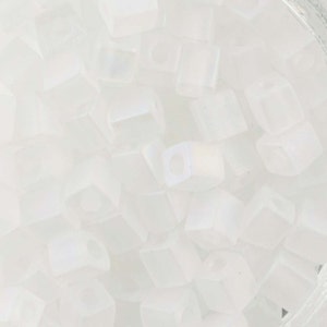 May include: A collection of opaque, white cube beads. Each bead has a square shape with a hole running through the center. The beads are scattered, creating a textured, light-reflecting surface. Ideal for jewelry making and crafts.