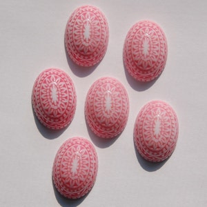 May include: Six pink oval-shaped cabochons with white intricate designs. The cabochons are smooth and glossy.