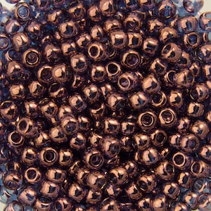 May include: A close-up image of a large quantity of small, round, iridescent purple glass beads. The beads have a metallic sheen and are arranged in a random pattern.