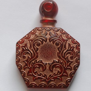 May include: A red glass perfume bottle with a gold-coloured embossed design. The bottle has a round stopper and a hexagonal base.