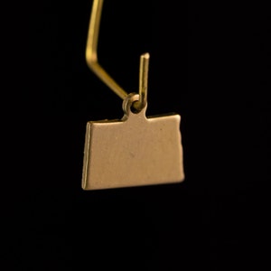 May include: Gold-colored metal charm shaped like the state of Wyoming. The charm is attached to a gold-colored metal loop.