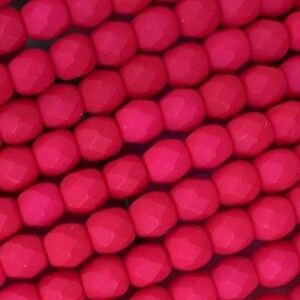 May include: A collection of vibrant hot pink beads arranged in parallel rows. Each bead features a multi-faceted, geometric surface with a matte finish, creating a uniform texture across the entire display of small, round, individual components.