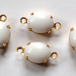 May include: Four white oval-shaped glass beads with gold metal settings and two loops on each side. The beads are perfect for jewelry making.