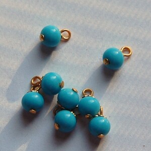 Op de afbeelding: Een groep van zeven turquoise blauwe kralen met gouden accenten. De kralen zijn rond en hebben een gladde afwerking. Ze zijn geregen aan een gouden ketting.