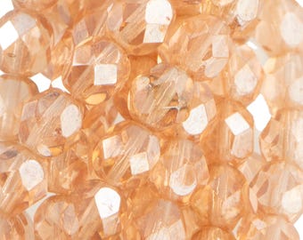 May include: Close-up of a pile of faceted, peach-colored beads. The beads have multiple flat surfaces that reflect light, creating a sparkling effect. These beads are suitable for jewelry making and crafting projects.