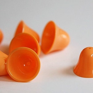 May include: Seven orange plastic bells, some are stacked on top of each other, and one is laying flat on a white surface.