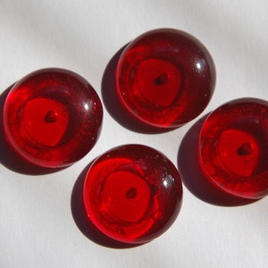 May include: Four round, red glass buttons with a small, clear centre. The buttons are shiny and have a slight raised edge.