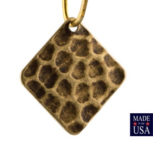 May include: A gold-toned, square-shaped pendant with a hammered texture. The pendant has a loop at the top for attaching to a chain or cord.