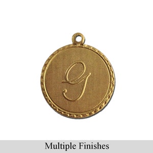 May include: Gold-toned metal charm with a cursive letter G in the center. The charm has a textured surface and a rope-like border.