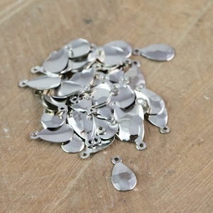 May include: A collection of shiny, silver-colored teardrop-shaped charms with small loops at the top for jewelry making. The charms have a hammered texture and are scattered on a light brown wooden surface.