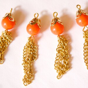 May include: Four orange and gold tassel charms with a decorative metal top. The tassels are made of gold chains.