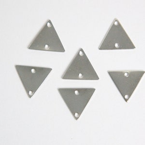 May include: Six silver triangle charms with a hole in the centre of each triangle. The charms are arranged in a symmetrical pattern on a white background.