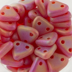 May include: A pile of small, triangular, iridescent pink beads with two holes each. The beads have a matte finish and are made of glass.