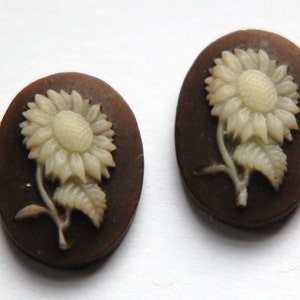 May include: A pair of brown oval-shaped cameo earrings with white sunflower designs.