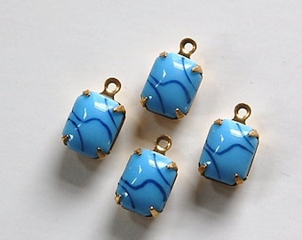 Puede incluir: Cuatro colgantes de vidrio azul con engastes de metal dorado. Cada colgante presenta un patrón azul en espiral.