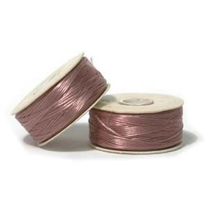 May include: Two spools of mauve-coloured cord. The cord is tightly wound around cardboard spools. The spools are positioned on a white surface, with one spool leaning against the other. The cord has a slight sheen.