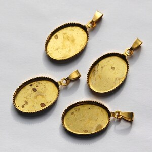 May include: Four gold-toned oval pendant trays with a decorative edge. The trays are empty and ready to be filled with resin, photos, or other embellishments.