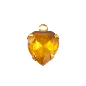 May include: A heart-shaped, faceted, amber-colored gemstone pendant with a gold-tone metal setting and a small loop at the top for hanging. The gemstone has a brilliant cut.
