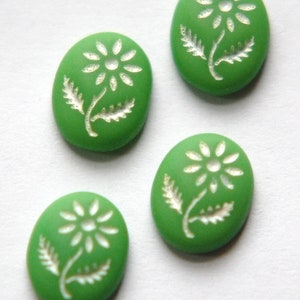 以下が含まれることがあります： 白いデイジーのデザインが施された緑色の楕円形のボタンが4つ。デイジーは白い中心と白い花びらで、縁はテクスチャ加工されています。