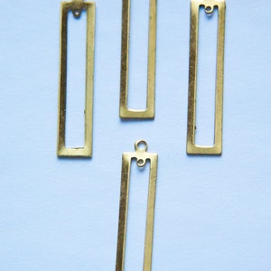 May include: Four gold-colored metal rectangular frames with a loop at the top. The frames are on a light blue background.