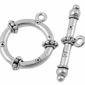 May include: A silver-toned toggle clasp set, featuring a circular ring with decorative beaded accents and a matching bar. The clasp is designed for jewelry making, with a classic and versatile style. The set is shown against a white background.