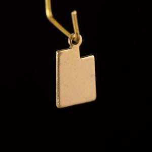 May include: Gold-colored earring with a square-shaped pendant.