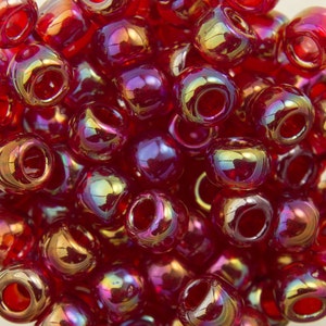 Puede incluir: Primer plano de un montón de cuentas de vidrio rojo iridiscente. Las cuentas son redondas y tienen una superficie brillante y reflectante.