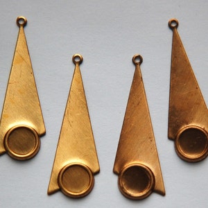 Puede incluir: Cuatro colgantes de metal de color dorado con forma triangular y una abertura redonda en la parte inferior. Cada colgante tiene un agujero en la parte superior para sujetar una cuerda o cadena.