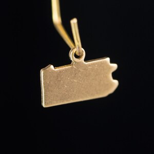 May include: A gold-colored charm shaped like the state of Pennsylvania. The charm is hanging from a gold chain.