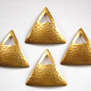 May include: Four gold-colored triangle-shaped metal charms with a small hole at the top. Each charm has a hammered texture and a smaller triangle cut out in the center.