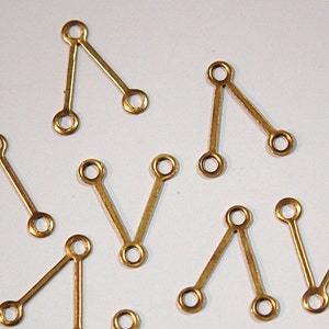May include: A group of ten gold-colored metal jump rings with a V-shaped design. Each ring has two loops at the top and one loop at the bottom.