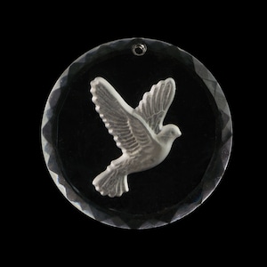 Könnte beinhalten: Ein klarer Glasanhänger mit einem silbernen Taubenmotiv. Die Taube ist im Flug und hat ihre Flügel ausgebreitet.